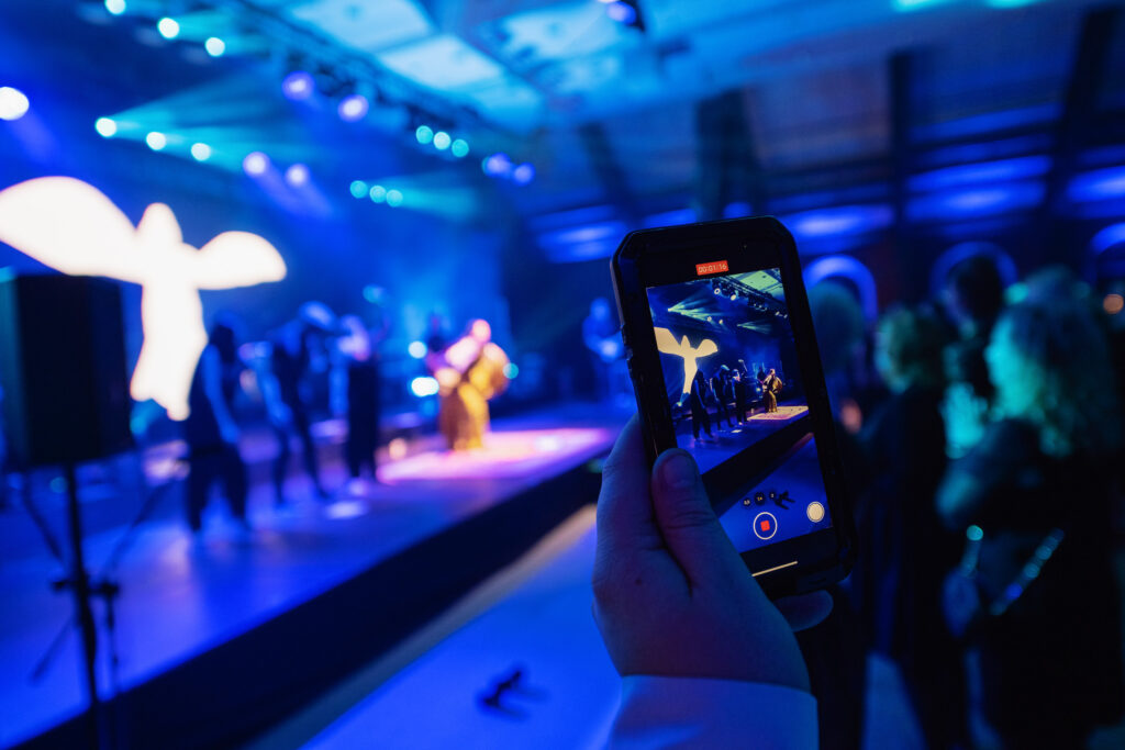 Obraz nagrywania telefonem koncertu podczas eventu firmowego w pełnej sali.